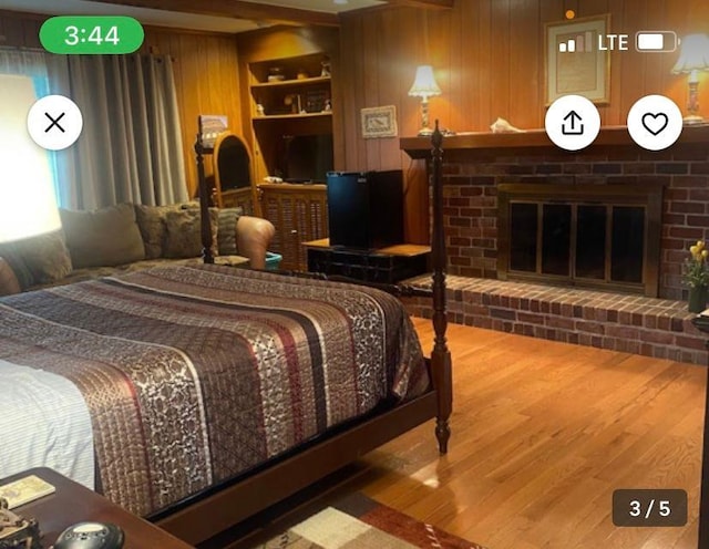 bedroom featuring a brick fireplace, wood-type flooring, and wood walls