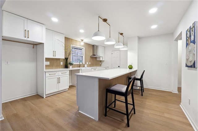 kitchen with pendant lighting, light hardwood / wood-style flooring, wall chimney exhaust hood, decorative backsplash, and white cabinetry