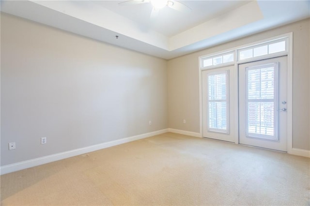 empty room featuring light carpet, ceiling fan, and a tray ceiling