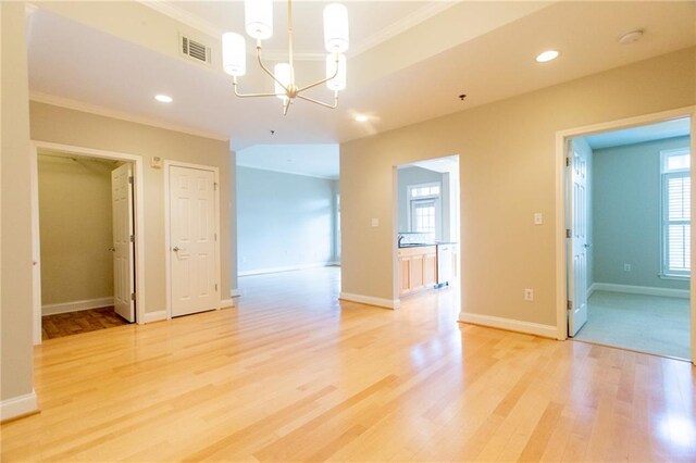 unfurnished room with light hardwood / wood-style flooring, crown molding, and a notable chandelier