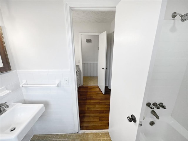 bathroom with tile walls, sink,  shower combination, and a textured ceiling