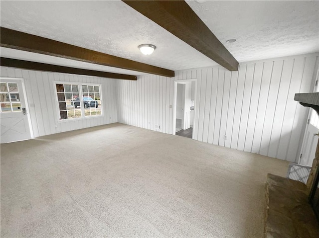 unfurnished living room with beamed ceiling, carpet flooring, and a textured ceiling