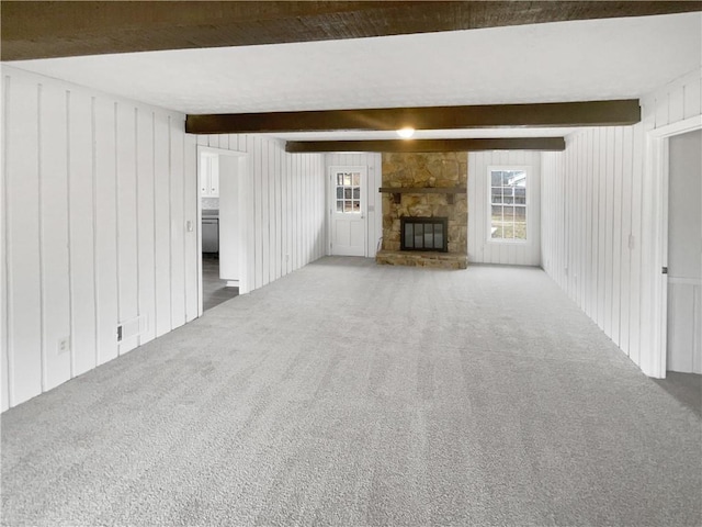 unfurnished living room with beamed ceiling, carpet flooring, and a stone fireplace