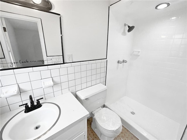 bathroom with a tile shower, vanity, tile walls, and toilet