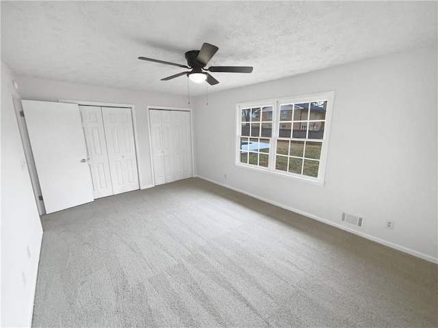 unfurnished bedroom with multiple closets, ceiling fan, carpet flooring, and a textured ceiling