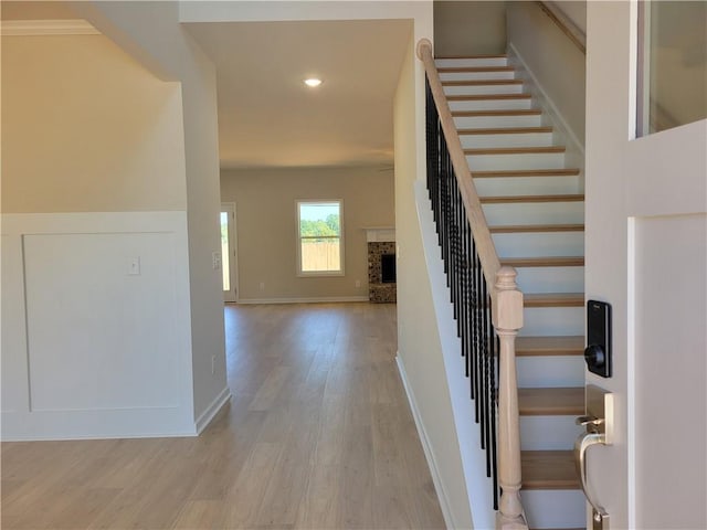 staircase with recessed lighting, a fireplace with raised hearth, baseboards, and wood finished floors