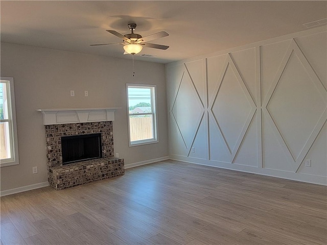 unfurnished living room with wood finished floors, visible vents, baseboards, a ceiling fan, and a brick fireplace