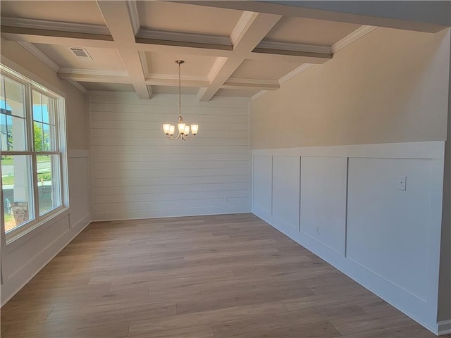 unfurnished room with beam ceiling, a decorative wall, an inviting chandelier, wood finished floors, and coffered ceiling