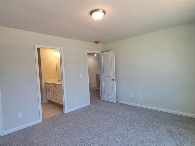 unfurnished bedroom with light carpet, baseboards, and ensuite bathroom