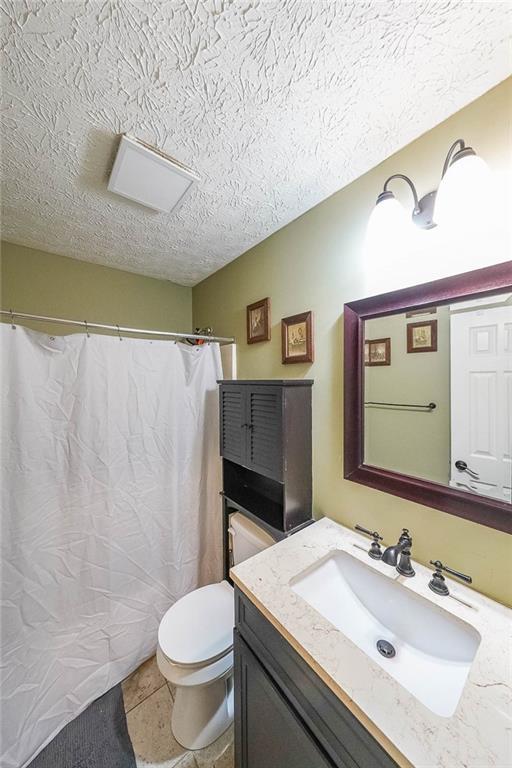 bathroom featuring vanity, toilet, tile patterned flooring, and a textured ceiling