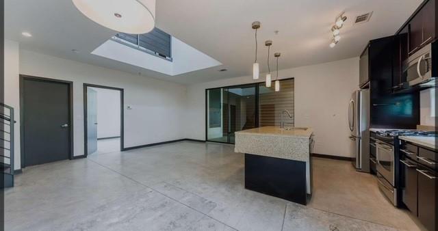 kitchen featuring appliances with stainless steel finishes, a skylight, a kitchen island with sink, sink, and hanging light fixtures