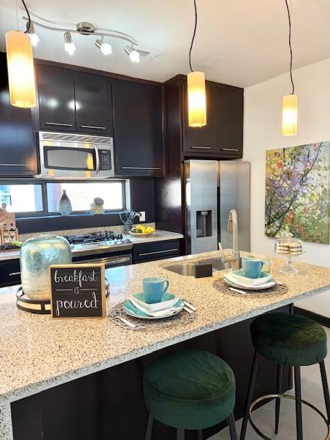 kitchen with a sink, a kitchen breakfast bar, hanging light fixtures, appliances with stainless steel finishes, and light stone countertops