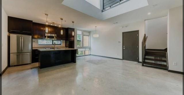 kitchen with sink, stainless steel fridge, an island with sink, decorative light fixtures, and dark brown cabinets