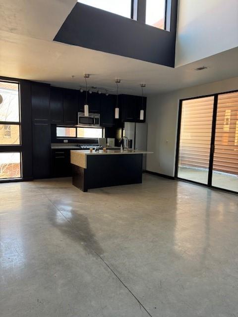 kitchen with hanging light fixtures, plenty of natural light, an island with sink, and appliances with stainless steel finishes