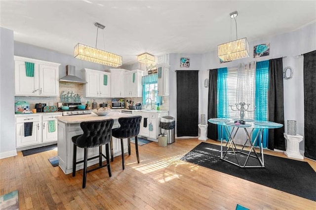 kitchen with wall chimney range hood, hanging light fixtures, a center island, and white cabinets