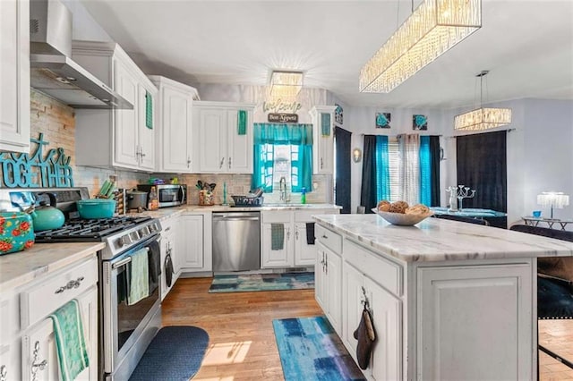 kitchen featuring stainless steel appliances, white cabinetry, a kitchen island, and wall chimney range hood