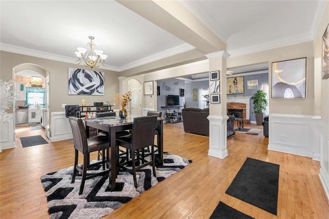 dining space with decorative columns, ornamental molding, a brick fireplace, and light hardwood / wood-style flooring