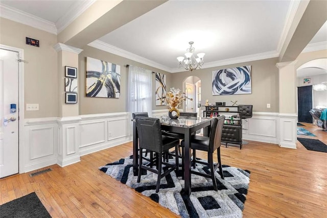 dining space with ornate columns, ornamental molding, a chandelier, and light wood-type flooring