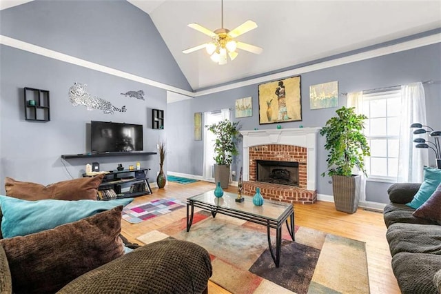 living room featuring ceiling fan, high vaulted ceiling, a brick fireplace, and light wood-type flooring