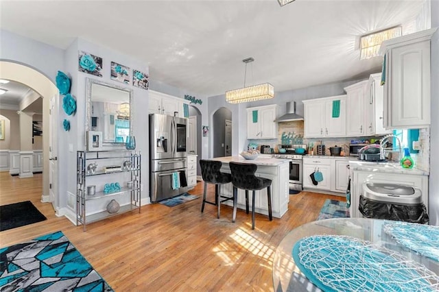 kitchen featuring wall chimney range hood, stainless steel appliances, white cabinets, and a kitchen island