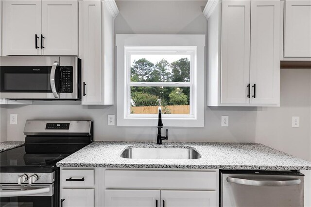 kitchen with sink, appliances with stainless steel finishes, hanging light fixtures, light stone countertops, and white cabinets