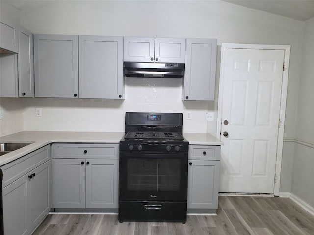 kitchen with light wood-style flooring, under cabinet range hood, light countertops, gray cabinets, and black gas range oven