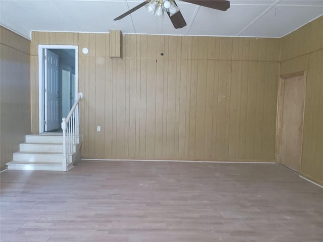 spare room with a ceiling fan, stairway, wood finished floors, and wood walls