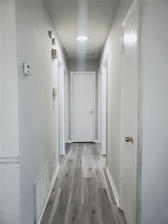 hall with baseboards, attic access, visible vents, and wood finished floors