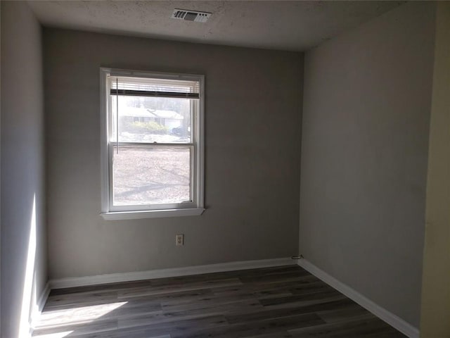 spare room with baseboards, visible vents, and wood finished floors