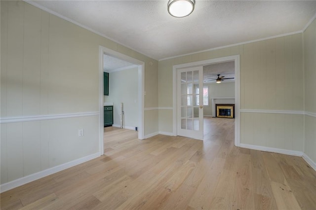 empty room with crown molding, french doors, a textured ceiling, and light wood-type flooring