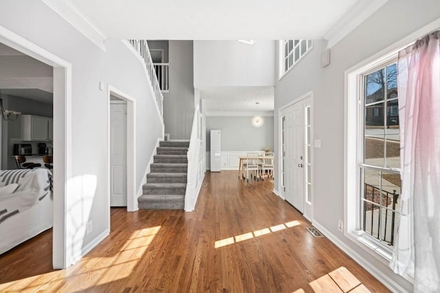 entrance foyer featuring visible vents, ornamental molding, wood finished floors, stairs, and a notable chandelier