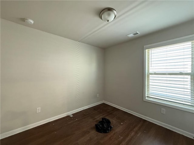 empty room featuring dark wood-style flooring, visible vents, and baseboards