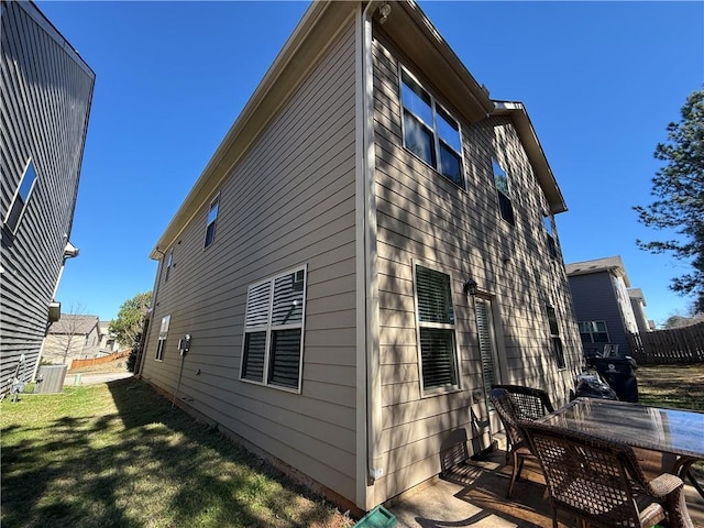 view of side of home featuring fence, outdoor dining area, and a lawn