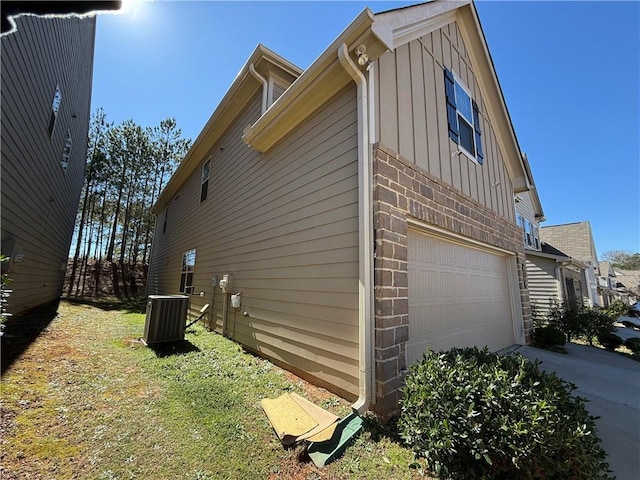 view of property exterior featuring an attached garage, cooling unit, board and batten siding, and brick siding