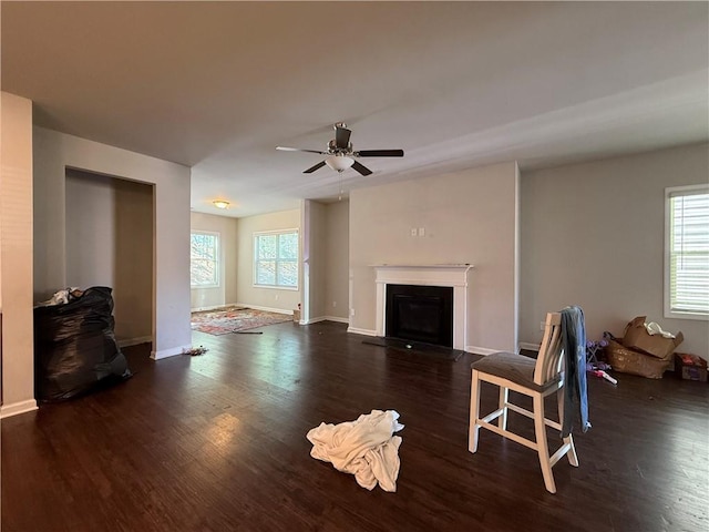 living area featuring ceiling fan, a glass covered fireplace, wood finished floors, and baseboards