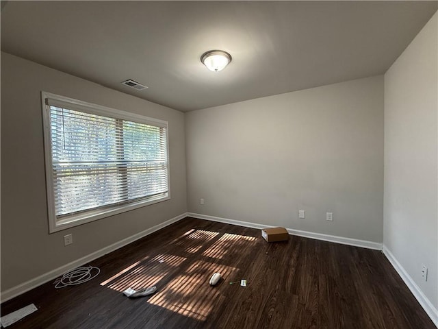 empty room featuring dark wood-type flooring, visible vents, and baseboards