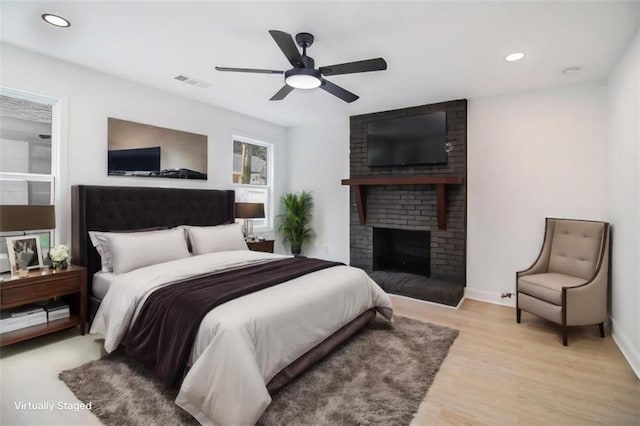 bedroom featuring ceiling fan, a brick fireplace, and light hardwood / wood-style flooring