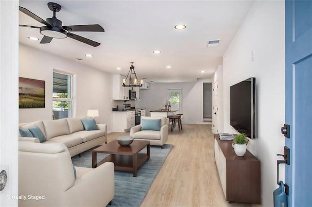 living room featuring a wealth of natural light, light hardwood / wood-style flooring, and ceiling fan with notable chandelier