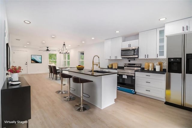 kitchen featuring white cabinetry, an island with sink, sink, decorative backsplash, and stainless steel appliances