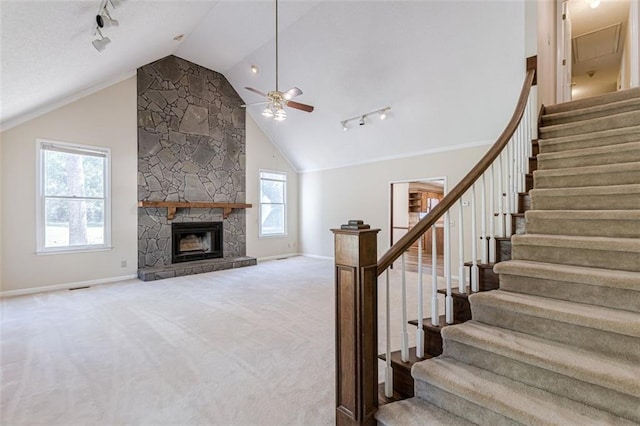 unfurnished living room featuring ceiling fan, track lighting, a stone fireplace, and light colored carpet