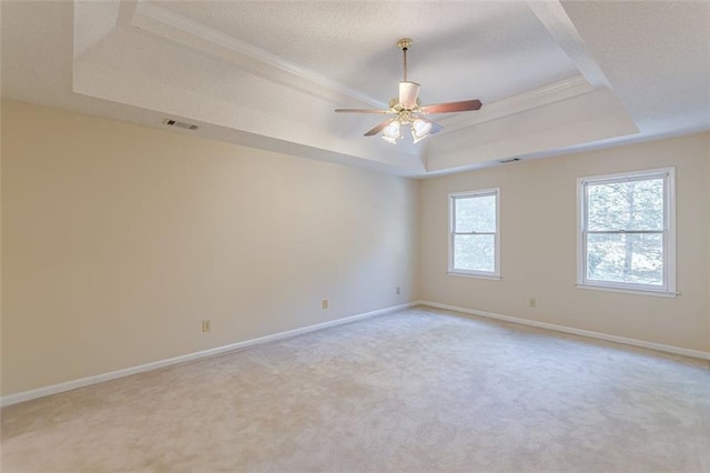 empty room with light colored carpet, ceiling fan, and a tray ceiling