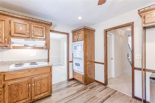 kitchen with white appliances, a textured ceiling, light wood-type flooring, ceiling fan, and light stone countertops