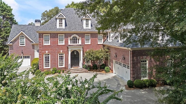 colonial-style house with concrete driveway, brick siding, an attached garage, and roof with shingles