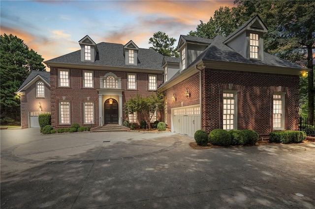 georgian-style home featuring a garage, concrete driveway, brick siding, and a shingled roof