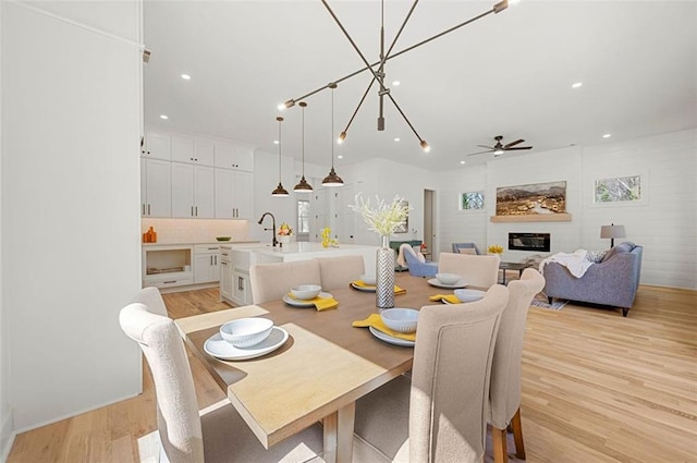 dining area with recessed lighting, a glass covered fireplace, light wood-style flooring, and ceiling fan with notable chandelier