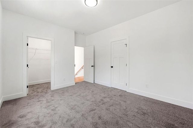 unfurnished bedroom featuring a closet, carpet flooring, a walk in closet, and baseboards