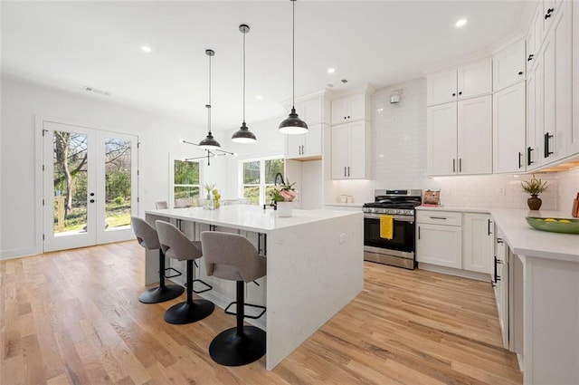 kitchen with backsplash, stainless steel electric range, white cabinetry, and light wood-style floors