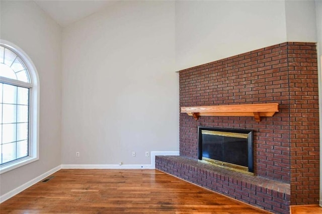 unfurnished living room featuring hardwood / wood-style floors, vaulted ceiling, and a brick fireplace