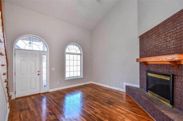 foyer featuring dark hardwood / wood-style flooring, high vaulted ceiling, and a brick fireplace