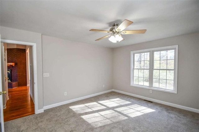 carpeted spare room featuring a fireplace and ceiling fan